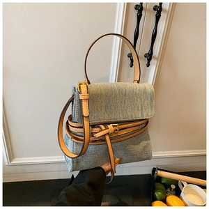 Close-up of light blue denim handbag with brown leather trim and gold buckle detail