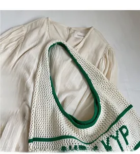Detail of crochet knit shoulder bag with green trim and woven text on beige fabric