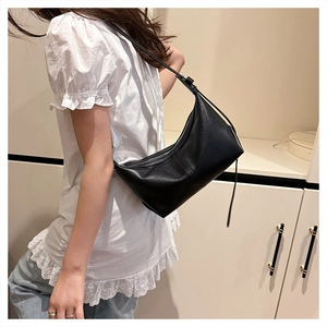 Close-up of a minimalist black hobo bag with a zipper and leather strap shown on a model
