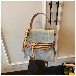 Close-up of light blue denim textured handbag with brown leather handles and straps