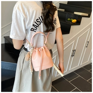 Pink drawstring bucket bag with textured leather, plush charm, and silk scarf detail