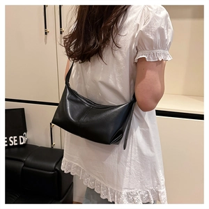 Detail of minimalist black leather crescent bag showing stitching and shoulder strap on model