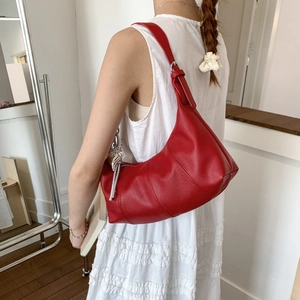 Red lychee-textured crescent bag with silver butterfly charm shown on white dress