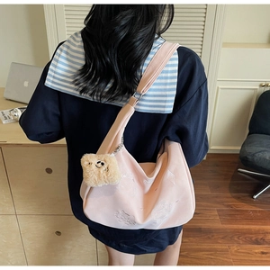 Detail of pink canvas crescent bag featuring cat embroidery and a plush bear charm
