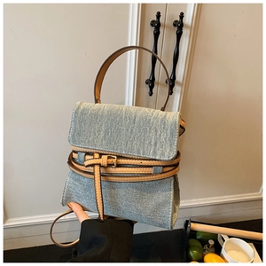 Detail of blue denim handbag featuring brown leather straps and metal buckle accents