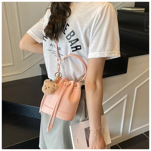 Detail view of light pink lychee texture leather bucket bag with cute plush bear charm