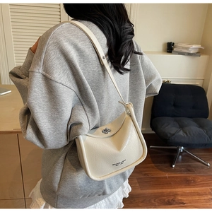 Side view of a creamy white glossy leather half-moon shoulder bag with metal turn-lock