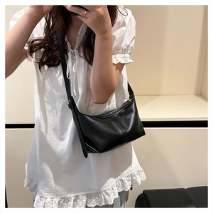 Mirror selfie showing a black crescent-shaped leather shoulder bag with adjustable strap