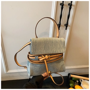 Detail of blue denim and tan leather tote bag with elegant gold buckle on a white door background