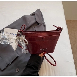 Detail of wine red pleated leather bucket bag featuring a pearl pendant and snap pocket
