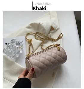 Gros plan d'un sac cylindrique matelassé kaki avec chaîne dorée sur fond blazer blanc