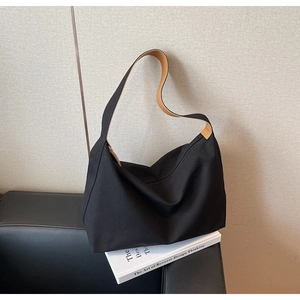 Dettaglio di una grande borsa tote in tela nera con manici marroni su un divano moderno