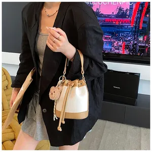 Detail of a white pebbled leather drawstring bucket bag with brown trim and bear charm