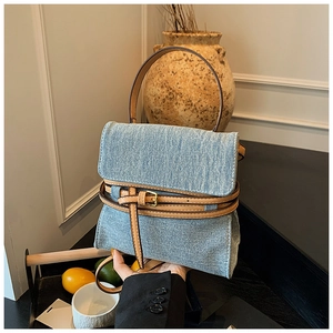 Detail of denim handbag with brown leather straps and gold metal buckle accents