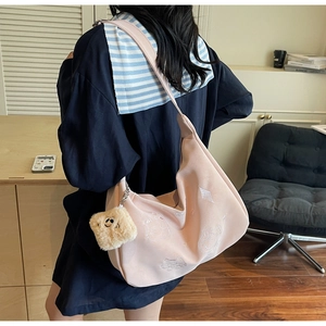 Pink canvas shoulder bag with cat embroidery and plush pendant worn by a model