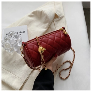 Détail du sac cylindrique matelassé rouge avec chaîne dorée sur un blazer de couleur crème