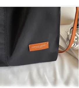 Detail of black fabric tote bag featuring leather logo tag and durable stitching
