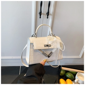 Close-up of white crocodile pattern Kelly bag with lace bow and pearl charm details