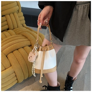 Close-up of stylish bucket bag with drawstring, white pebble leather and bear charm