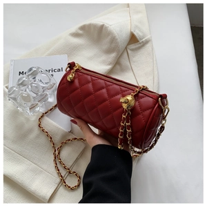 Détail d'un sac cylindrique matelassé bordeaux avec chaîne dorée et boucle sphérique