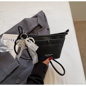 Detail of black textured bucket bag with white lace pearl bow and branding logo