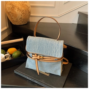 Detail of light blue denim tote bag with brown leather handles and buckle strap decor