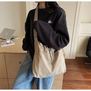 Detail view of a large beige nylon bucket bag with drawstring and side pocket