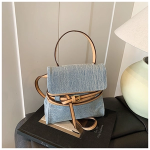 Detail of light blue denim textured crossbody bag with brown leather trim and gold buckle