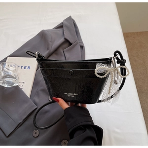 Detail of black glossy wrinkled leather bag with pearl bow charm and lace trim