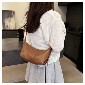 Brown leather crescent bag detail showing stitching and crossbody strap on model