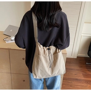 Macro view of beige nylon bucket bag with black drawstring closure and wide shoulder strap
