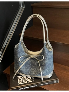 Denim patchwork underarm bag with silver bow detail and metallic straps on a wooden step