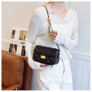 Detail of a black quilted mini crossbody bag with a gold lock and chain strap
