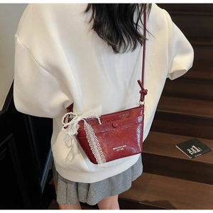 Detail of red patent leather crossbody bag with white lace bow and pearl pendant charm
