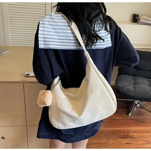 Close-up of white crossbody hobo bag with cat embroidery and plush cat charm accessory