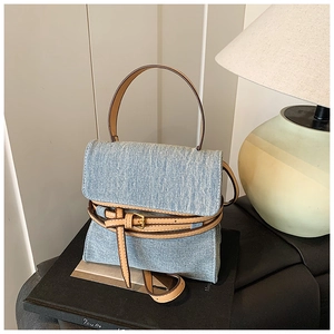 Detail view of light blue denim handbag with brown leather trim and golden buckle