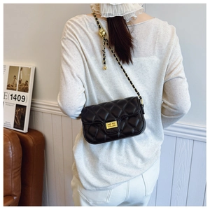 Rear view of model wearing a black quilted crossbody bag with gold chain strap detail