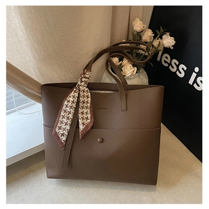 Detail of dark brown leather tote bag featuring a textured finish and stylish plaid scarf