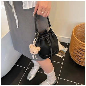 Detail of black leather bucket bag with white stitching and plush bear charm