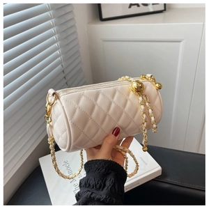 Détail du sac cylindrique matelassé crème avec chaîne dorée et pendentif sphérique