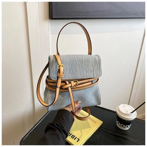 Detailed close-up of a blue denim tote bag featuring brown leather straps and gold buckle
