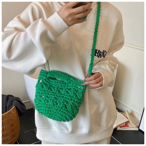 Detail view of a green hand-woven knit bucket bag styled on a white sweatshirt