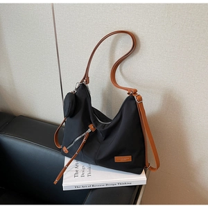 Close-up of black nylon tote bag featuring brown leather straps and small coin purse