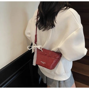 Detail view of burgundy leather bag with lace bow and pearl strap on white hoodie