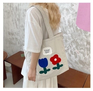 Detail view of canvas tote bag featuring floral plush patches and embroidered slogan label