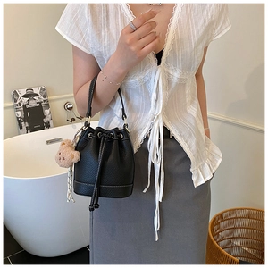 Detail of black leather bucket bag with white contrast stitching and a cute bear charm