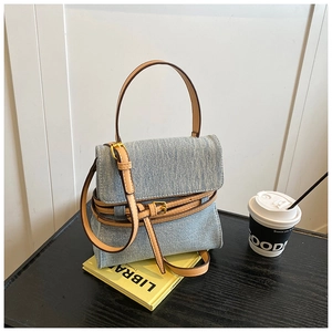 Detail of light blue denim handbag featuring brown leather handles and gold metal buckles