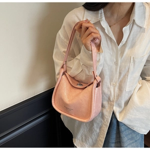 Close-up of light pink pleated leather crossbody bag with silver clasp on white shirt