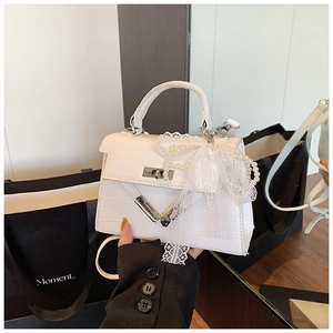 Detail of white crocodile texture handbag with lace bow and pearl chain accent