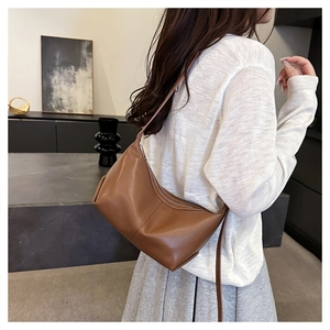 Brown geometric leather shoulder bag shown on model with minimalist modern interior design